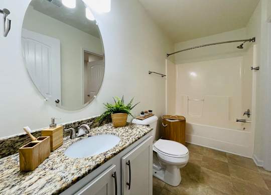 A bathroom with a marble countertop and a round mirror.