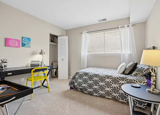 A bedroom with a bed, desk, chair, and a framed picture on the wall.