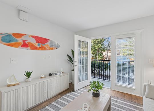 A living room with a white couch, a coffee table, and a surfboard artwork on the wall.