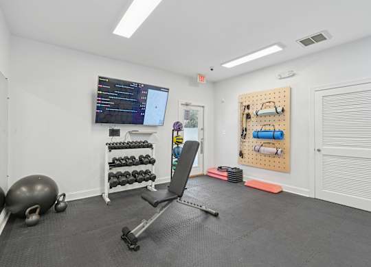 A gym room with a bench, weights, and a screen.
