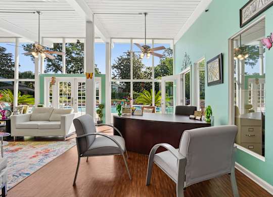 A room with a desk and chairs with a view of the backyard.
