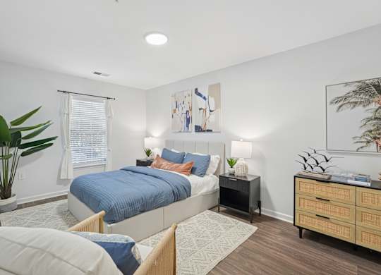 A bedroom with a bed, nightstand, and a plant.