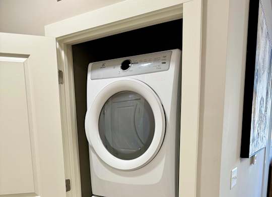 A white front load washing machine is in a white door at The Collective Upper Westside Apartments, Georgia, 30318