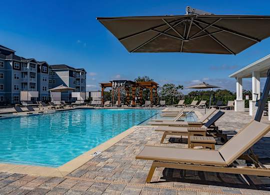 A pool with sun loungers and a building in the background at The Waverly at Winter Haven Apartments, Florida, 33884
