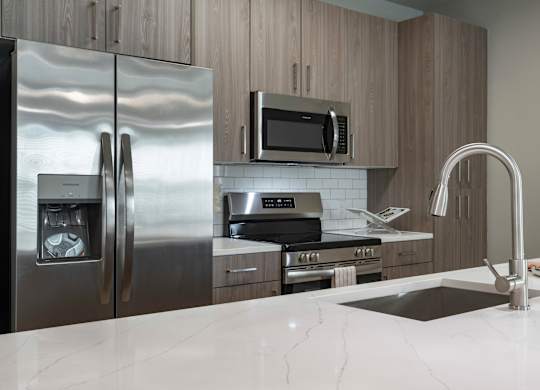 A modern kitchen with a stainless steel refrigerator, microwave, and oven at The Waverly at Winter Haven Apartments, Florida, 33884