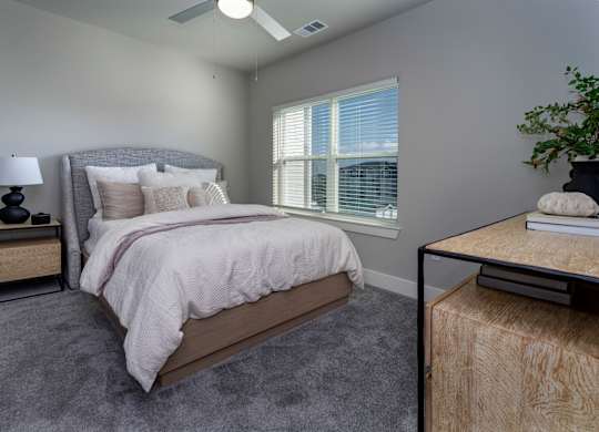 A bedroom with a large bed, a nightstand with a lamp, and a window with blinds at The Waverly at Winter Haven Apartments, Florida, 33884
