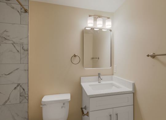 A bathroom with a toilet, sink, mirror and a towel bar.