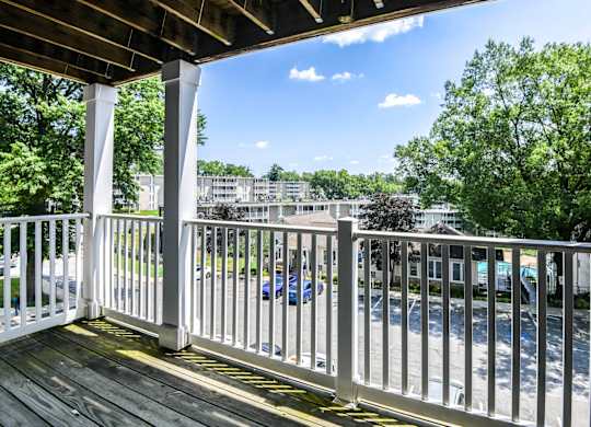 A white railing on a wooden deck overlooks a parking lot.