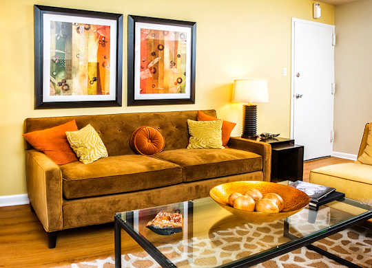 A brown couch with a glass coffee table in front of it.