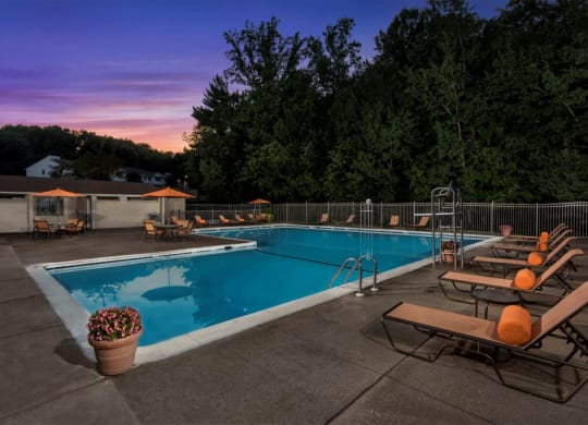 a swimming pool with chairs around it at sunset