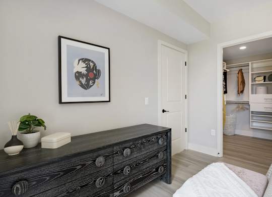 A black dresser with a framed picture above it and a small potted plant on top.