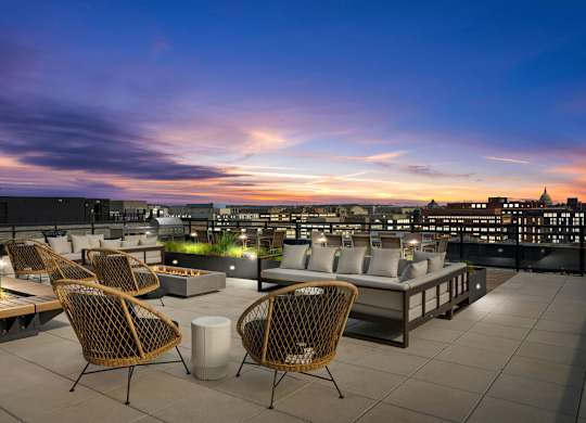 A rooftop patio with chairs and a table overlooking a city skyline at dusk.
