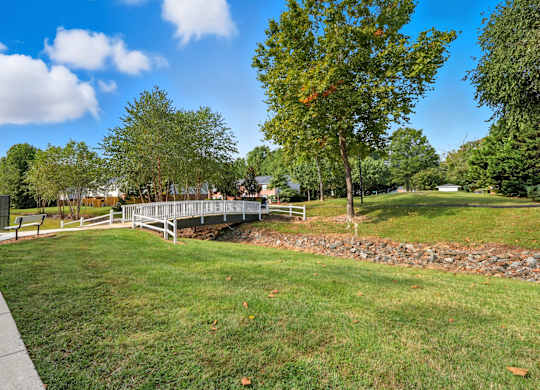 A park with a bridge, trees, and a clear sky.