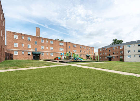 A playground in the middle of a grassy courtyard surrounded by brick buildings.