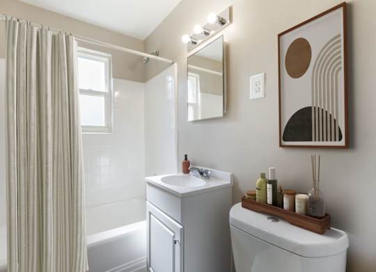 A bathroom with a white toilet, a white sink, a white bathtub, a mirror, and a picture on the wall.