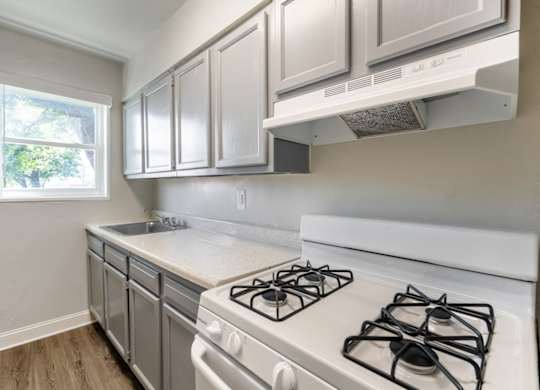 A kitchen with a white stove top oven and white cabinets.