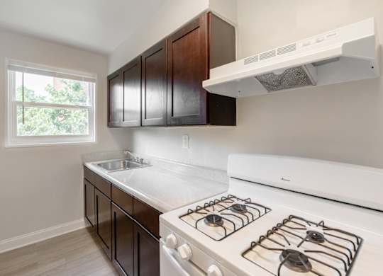 A kitchen with a white stove top oven and dark brown cabinets.