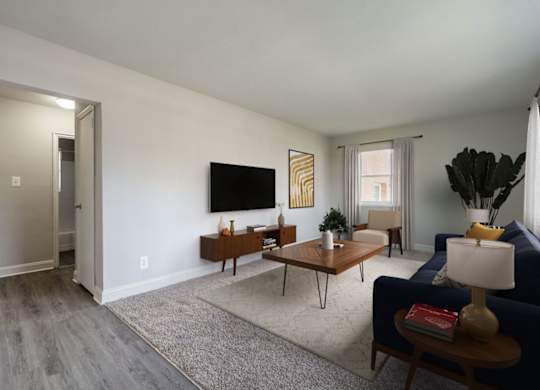 A living room with a blue couch, a wooden coffee table, and a flat-screen TV mounted on the wall.