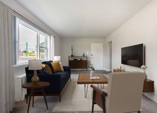 A living room with a blue couch, a wooden coffee table, and a flat screen TV mounted on the wall.