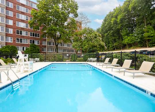 A large swimming pool with lounge chairs and a building in the background.