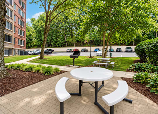 A white picnic table with two benches is in the middle of a brick patio.