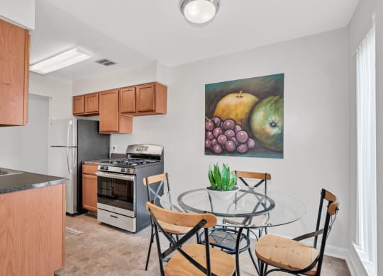 a dining area with a glass table and chairs and a kitchen in the background