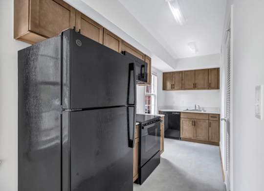 A black refrigerator stands in a kitchen with wooden cabinets and a white wall.