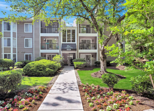 a walkway in front of an apartment building with trees and grass