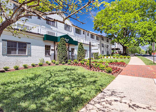 A white building with a green awning is surrounded by trees and shrubs.