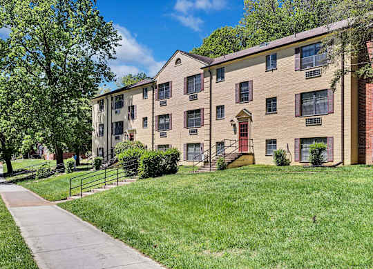 A brick apartment building with a red door and a green lawn in front.