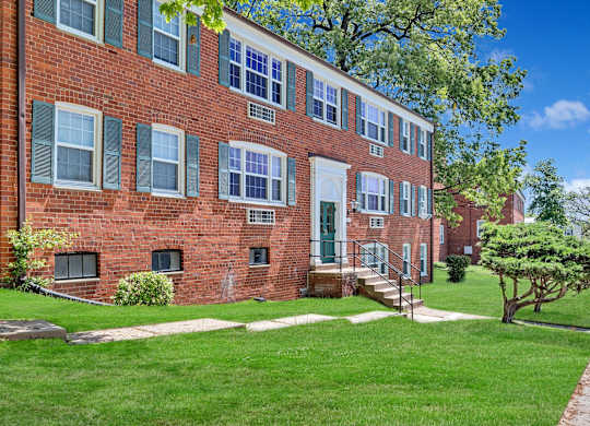 A red brick building with green shutters and a tree in front.