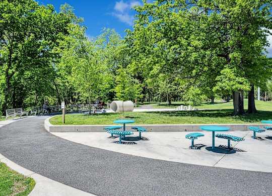 A park with a paved walkway, picnic tables, and trees.
