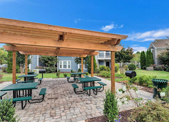 a cobblestone picnic area with seating and pergola.