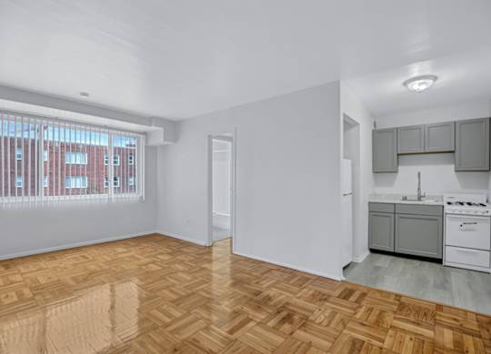 A room with wooden flooring and a kitchen area to the right.