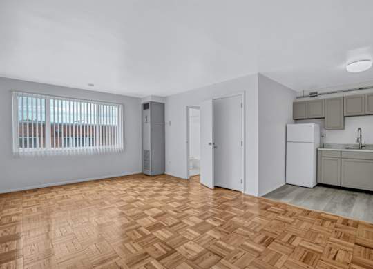 A room with wooden flooring and a kitchen area in the background.