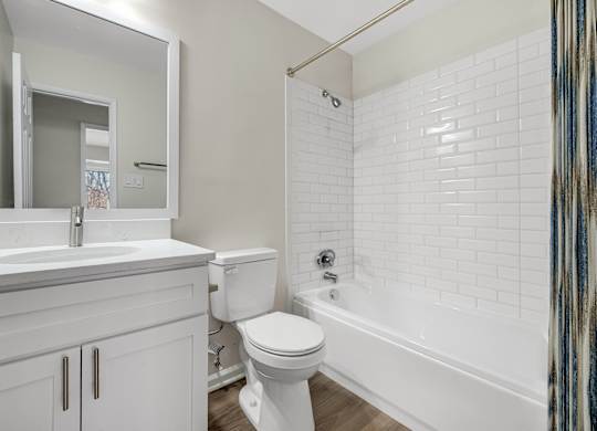 A bathroom with a white toilet and a shower with white subway tile backsplash curtain with a blue and brown pattern.