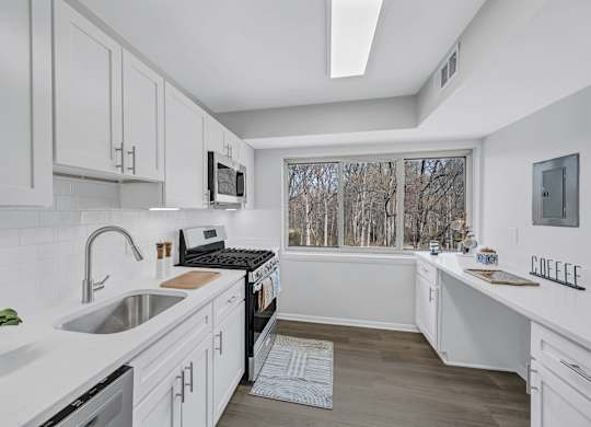 A kitchen with white cabinets and a window overlooking trees.