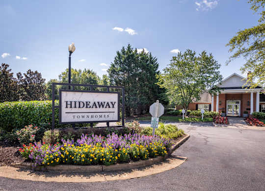 A sign for Hideaway Townhomes is in front of a house.