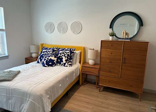 A bedroom with a bed, nightstand, and a dresser with a mirror on top.