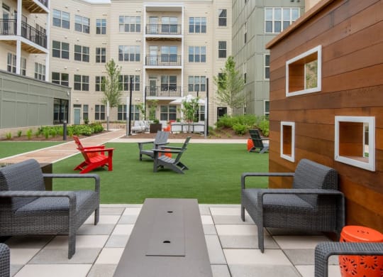 an outdoor lounge area with chairs and tables in front of an apartment building