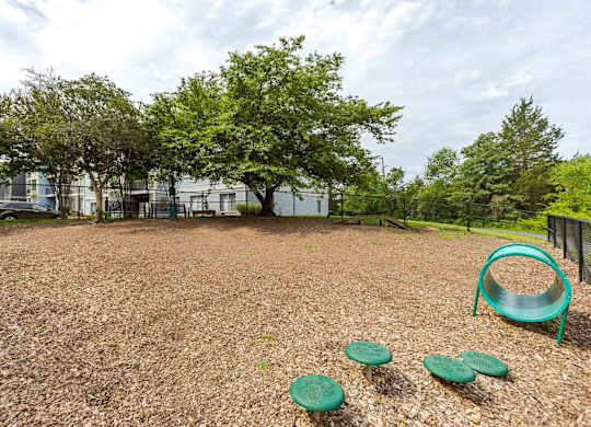A playground with a green slide and three green plastic discs on a brown surface.