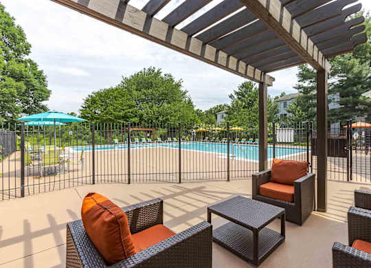 A patio with a pool in the background and a black table and chairs.