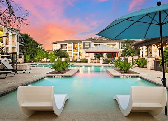 a swimming pool with two white chairs and an umbrella