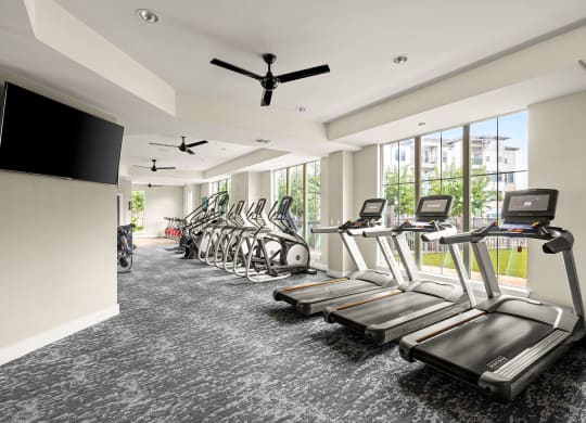 a gym with cardio machines and a tv