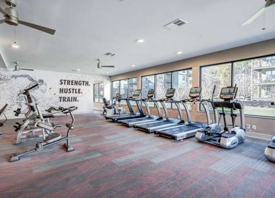 A gym with a variety of equipment including treadmills, elliptical machines, and a wall mural that reads