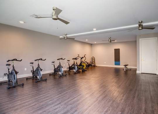 A room with a wooden floor and a wall of exercise bikes.