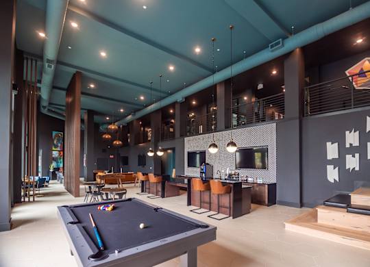 A pool table is in the middle of a room with a bar and a TV.