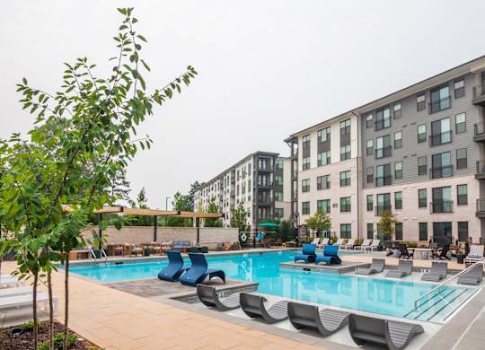 a swimming pool with lounge chairs in front of apartment buildings