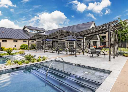 A pool area with a hot tub and a building in the background.
