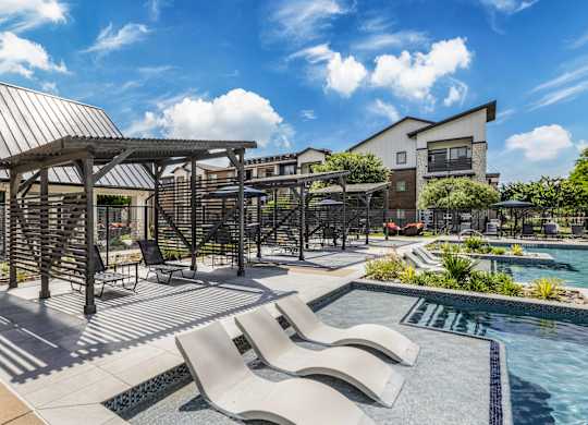 A pool area with a metal pergola and lounge chairs.